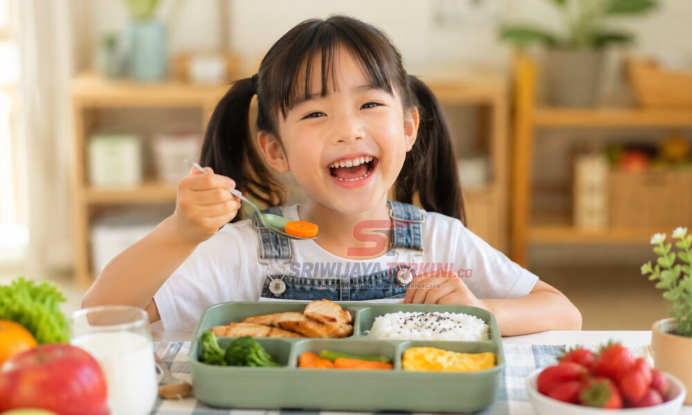 Seorang anak menikmati menu makan siang sehat berisi nasi, ayam, sayuran, telur, dan buah di meja makan dengan suasana ceria. (Foto: dok sriwijayaterkini.co)